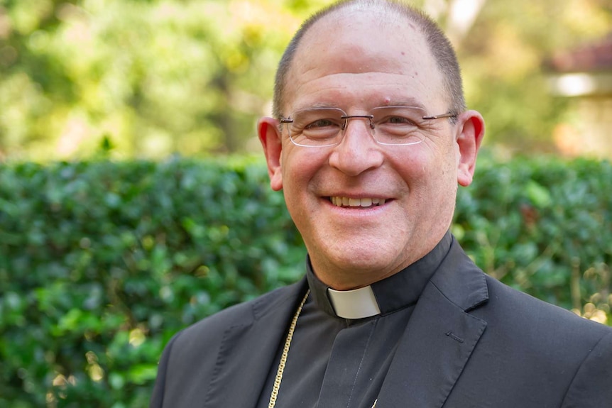 A smiling man wearing a priest's collar and large gold crucifix.