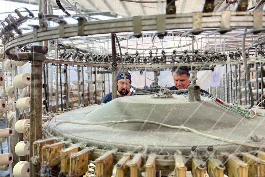 Two men can be seen standing behind a large knitting machine.