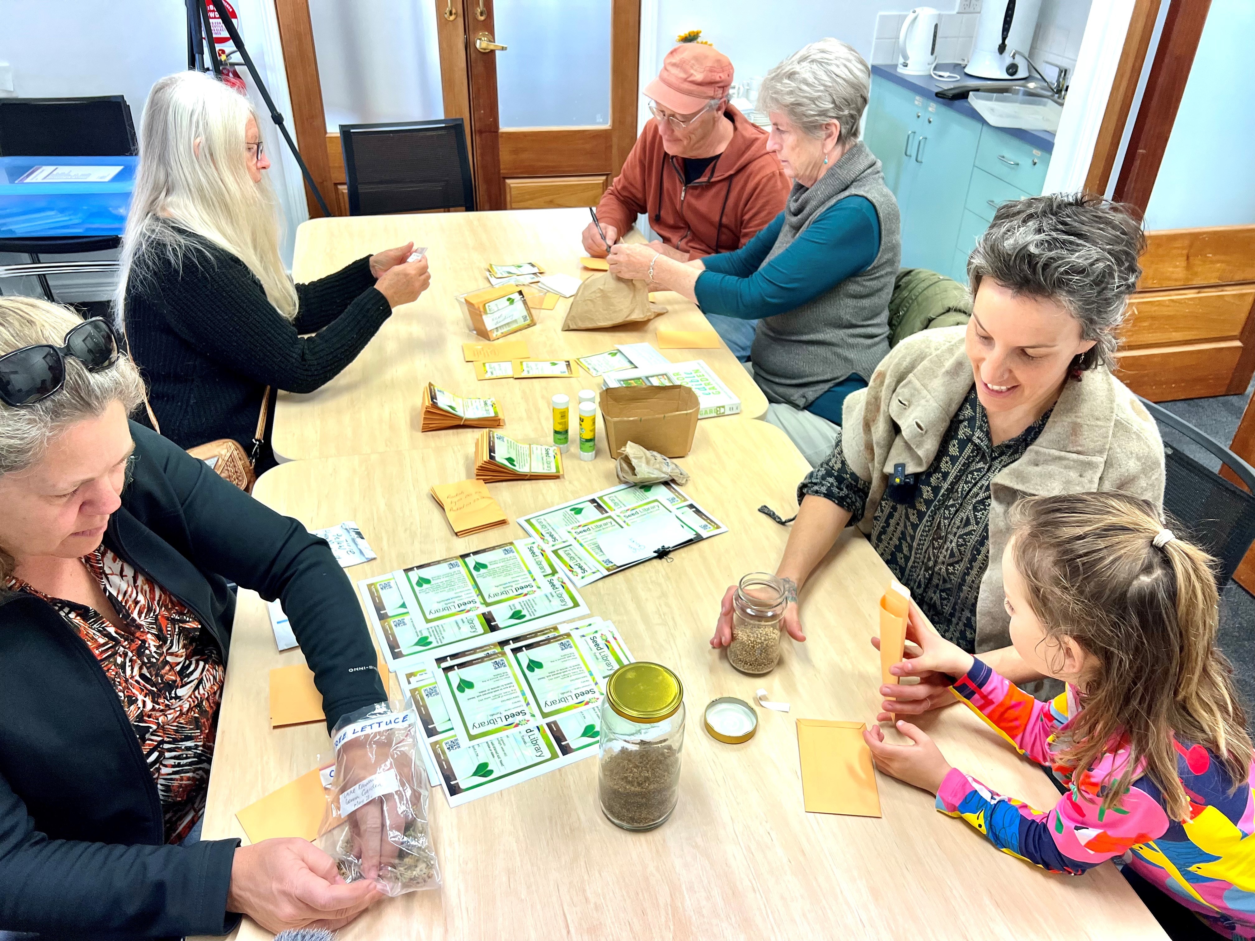 People sit at a table putting seeds in packets and writing the plants names on the labels.