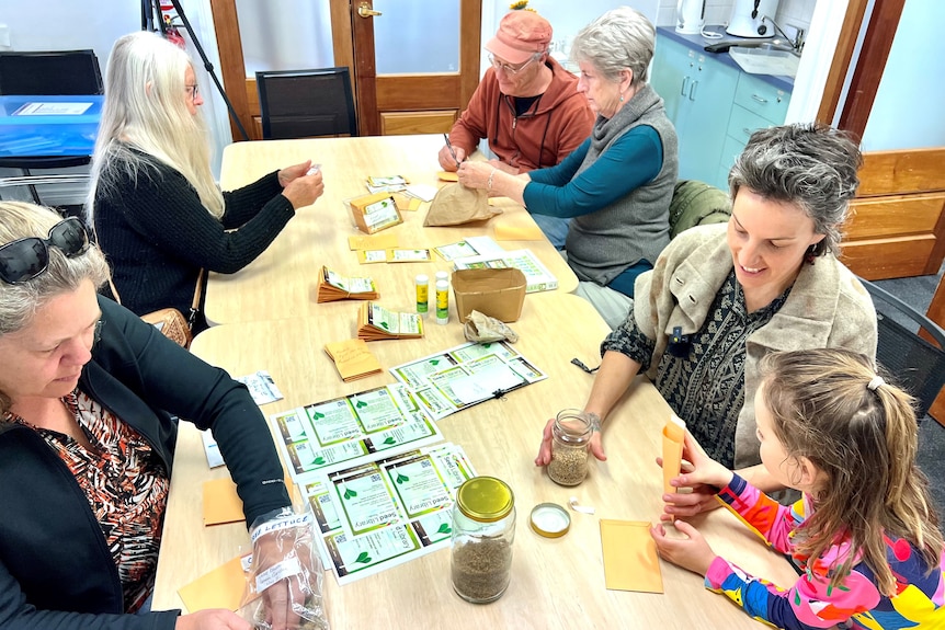 People sit at a table putting seeds in packets and writing the plants names on the labels.