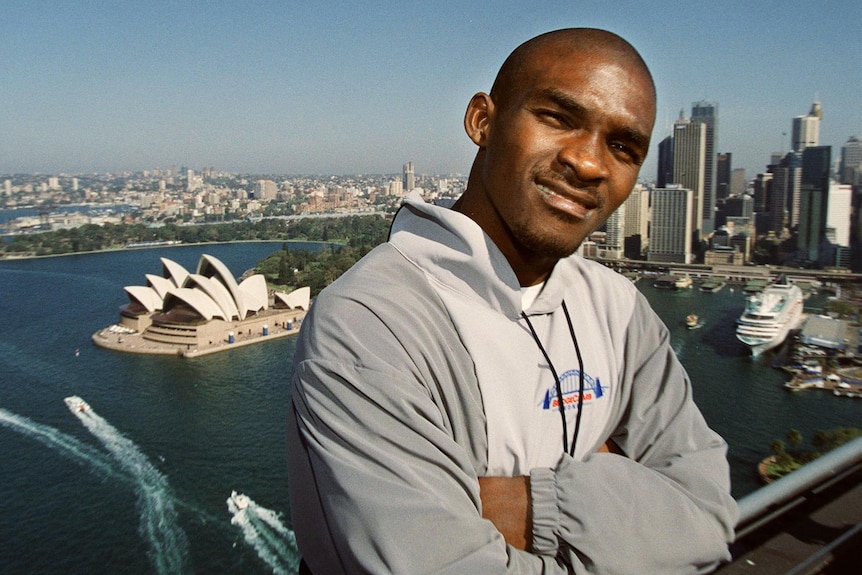 Eric Moussambani standing against the backdrop of Sydney Harbour with the Opera House in view