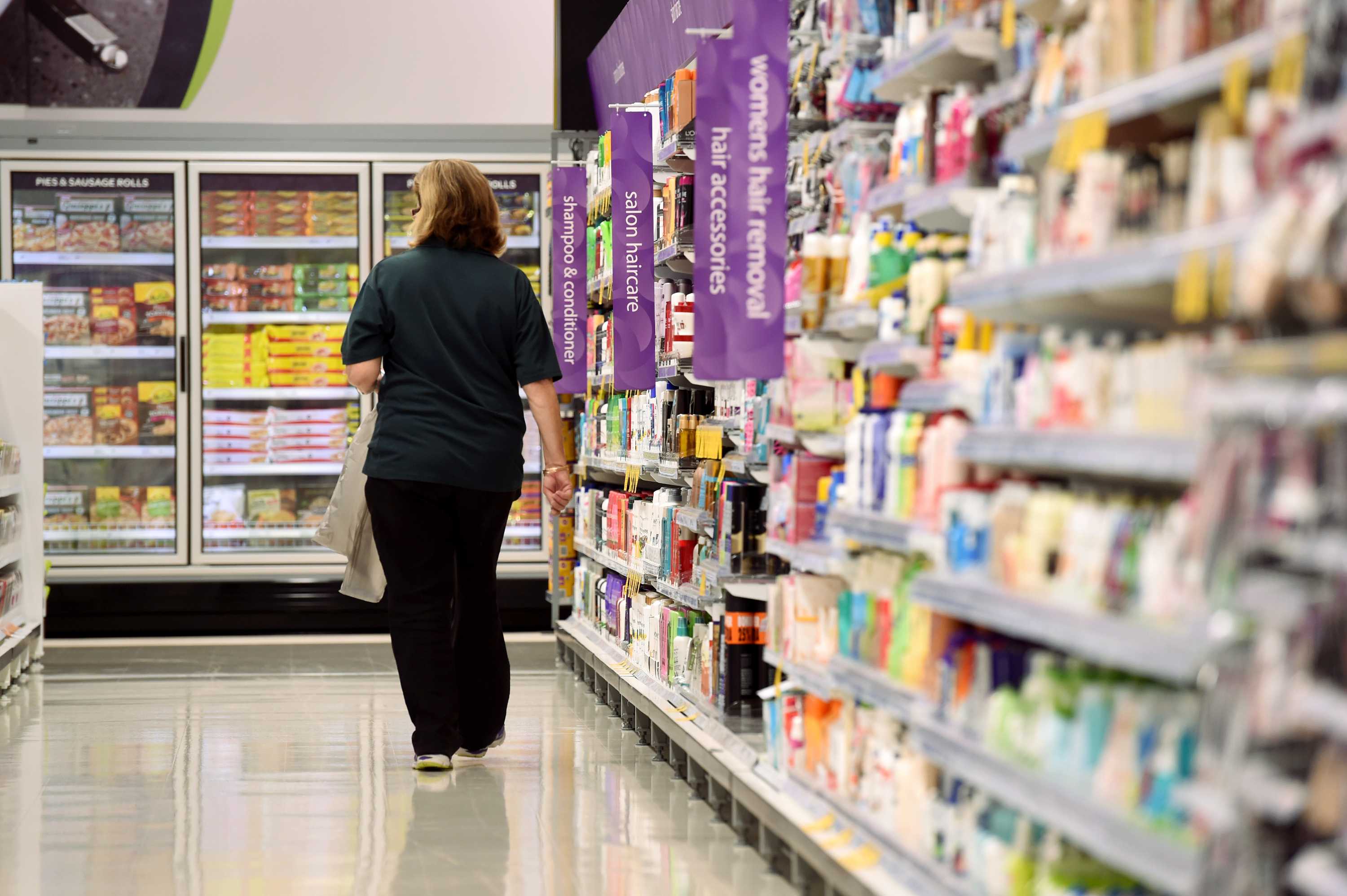 A woman walks down an aisle of a supermarket. Products on shelves either side of her.