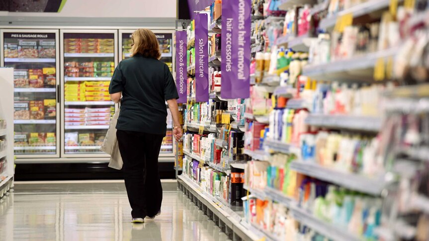 A woman walks down an aisle of a supermarket. Products on shelves either side of her.