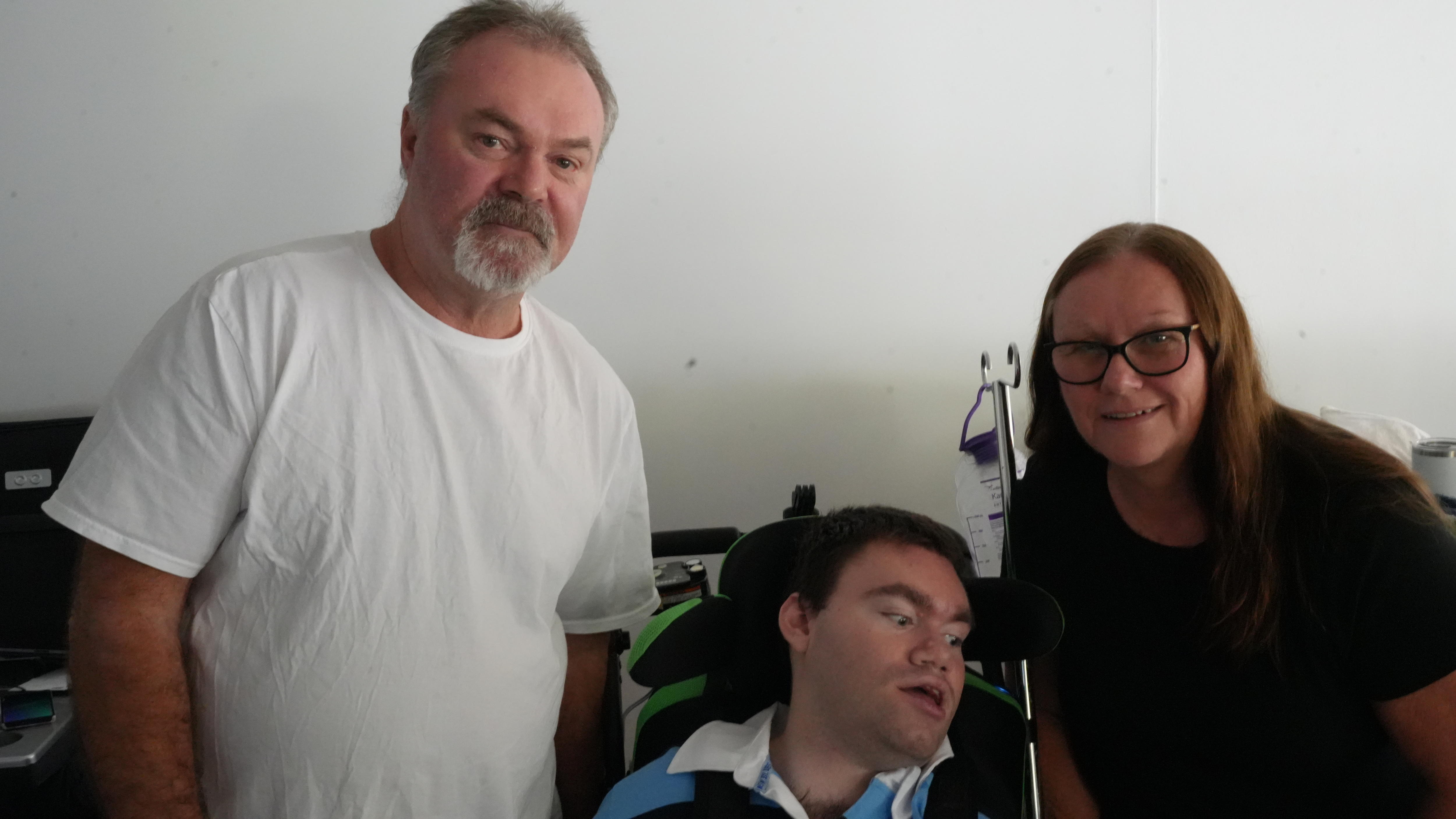 A man standing, another man sitting in an electric chair and a woman smiling