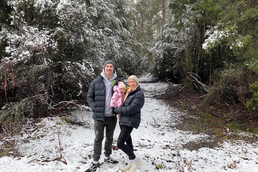 Sarah, Luke and Halle stand together smiling in a lightly snow-covered forest