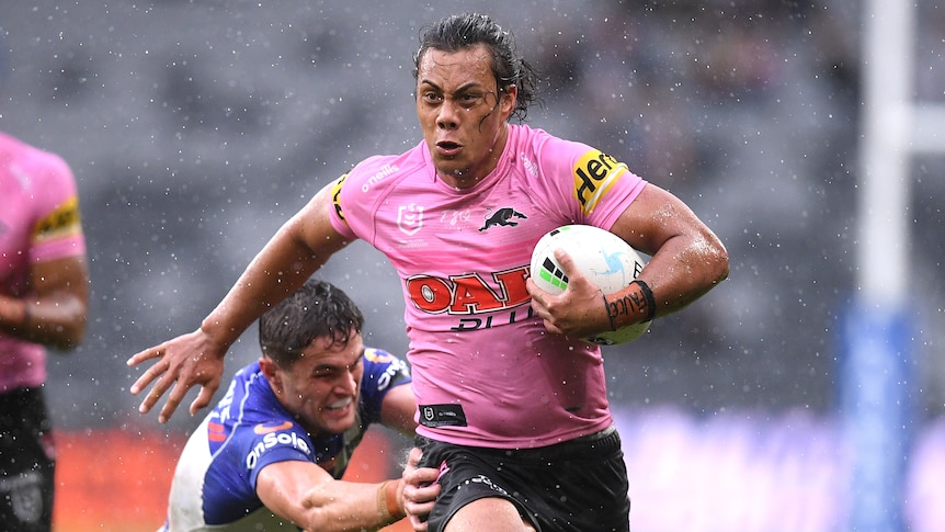 Penrith Panthers' Jarome Luai runs with the football in the rain. Bulldogs' Kyle Flanagan dives to try to tackle him.