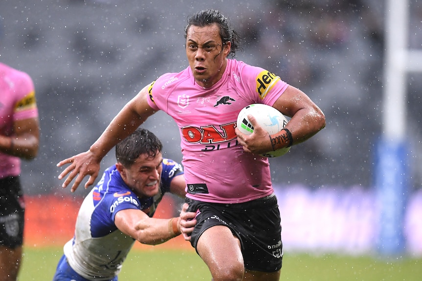 Penrith Panthers' Jarome Luai runs with the football in the rain. Bulldogs' Kyle Flanagan dives to try to tackle him.