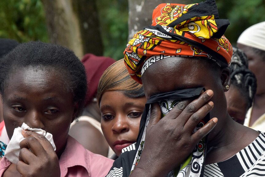 One woman in a head scarf covers her face as another holds a handkerchief to her nose at a Kenyan primary school.