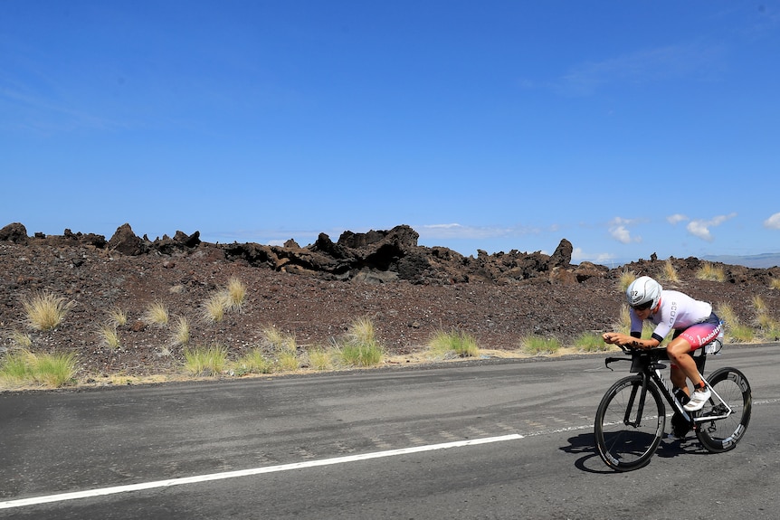 Sarah Crowley rides her time trial bike on a road next to bare rock