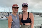 Two girls in athletic wear stand in front of a marina of boats.