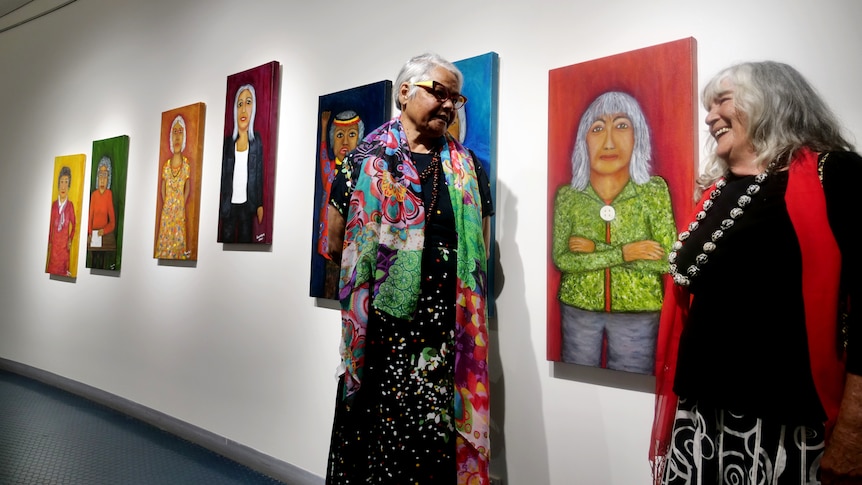 Two women smiling at each other in an art gallery