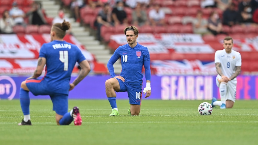 Jack Grealish kneels wearing a blue soccer kit
