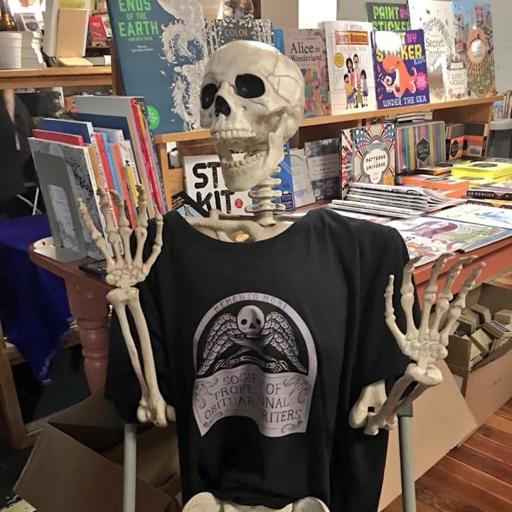Skeleton wearing black t-shirt with Society of Professional Obituary Writers logo on front