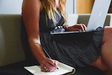 A young woman with a laptop computer takes notes.