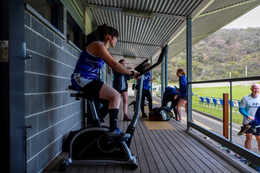 Woman in sportswear on fitness bike next to football ground