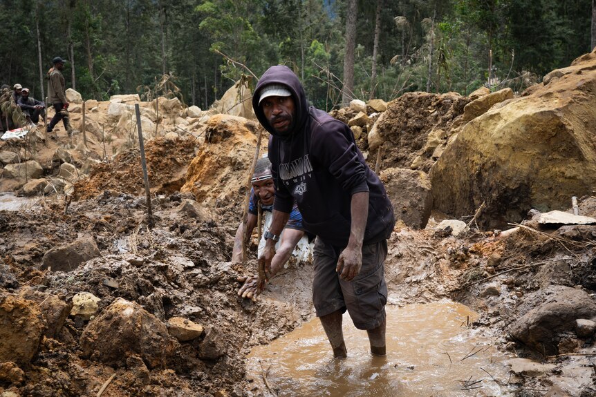 A man standing in a puddle of murky water in a muddy area