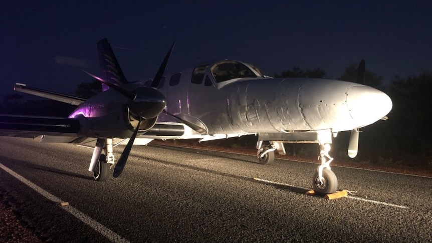 A small plane sits undamaged in the middle of a remote highway at night time.