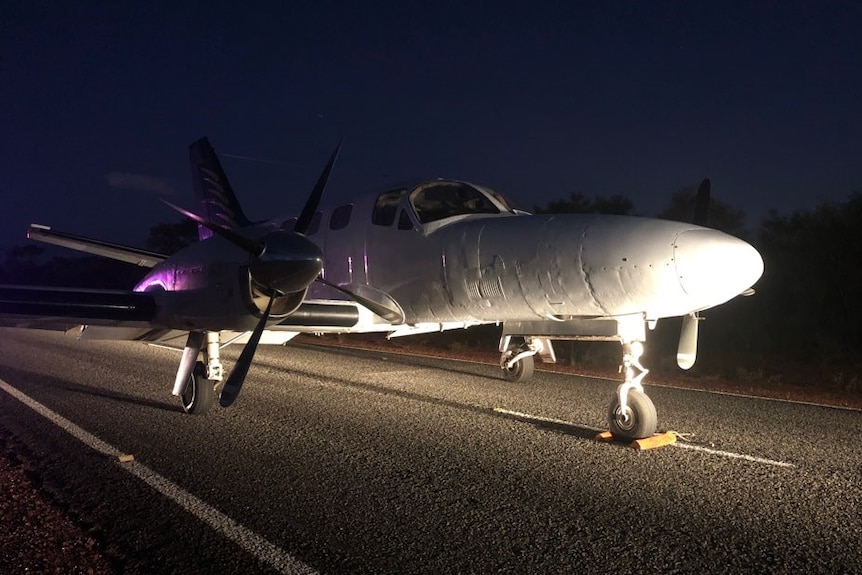 A small plane sits undamaged in the middle of a remote highway at night time.