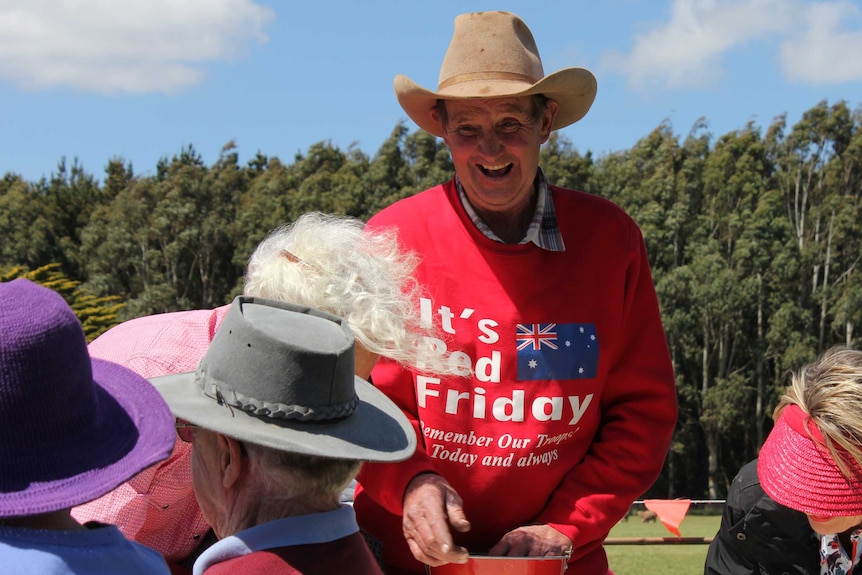 A man wearing a red jumper and cowboy hat laughing with four people around him.