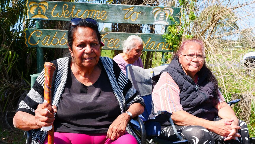 Aunty Susan Anderson sitting with other elders in front of Cabbage Tree Island welcome sign