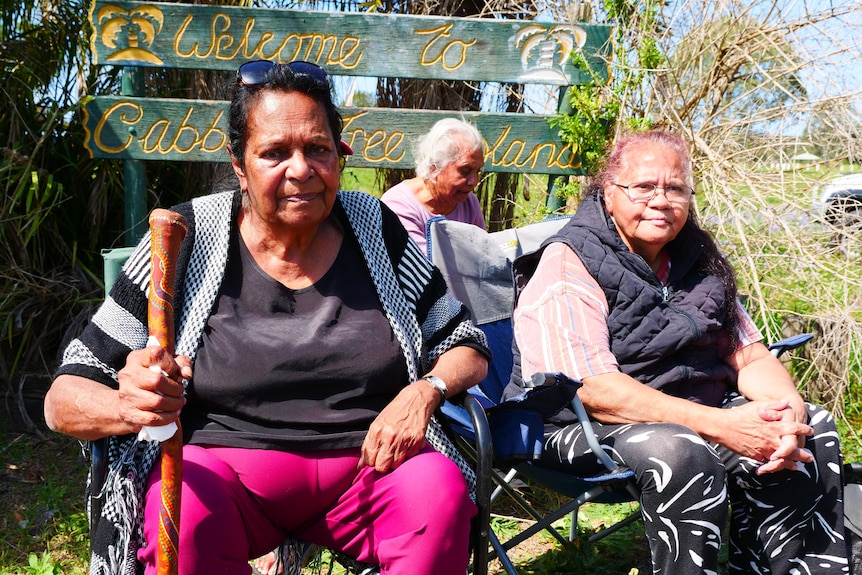 Aunty Susan Anderson sitting with other elders in front of Cabbage Tree Island welcome sign