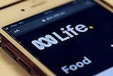 ABC Life mobile website is seen on a white iPhone resting on a white desk. The ABC Life logo is white, the page is black.