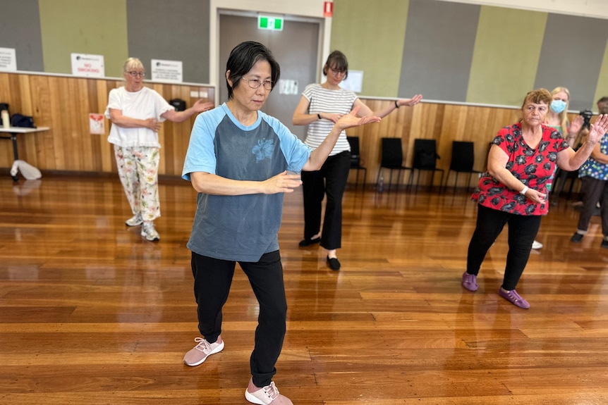 Four older women do tai chi in a community hall.