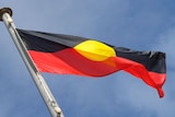 An Aboriginal flag flying at the top of a flag post against a blue sky.