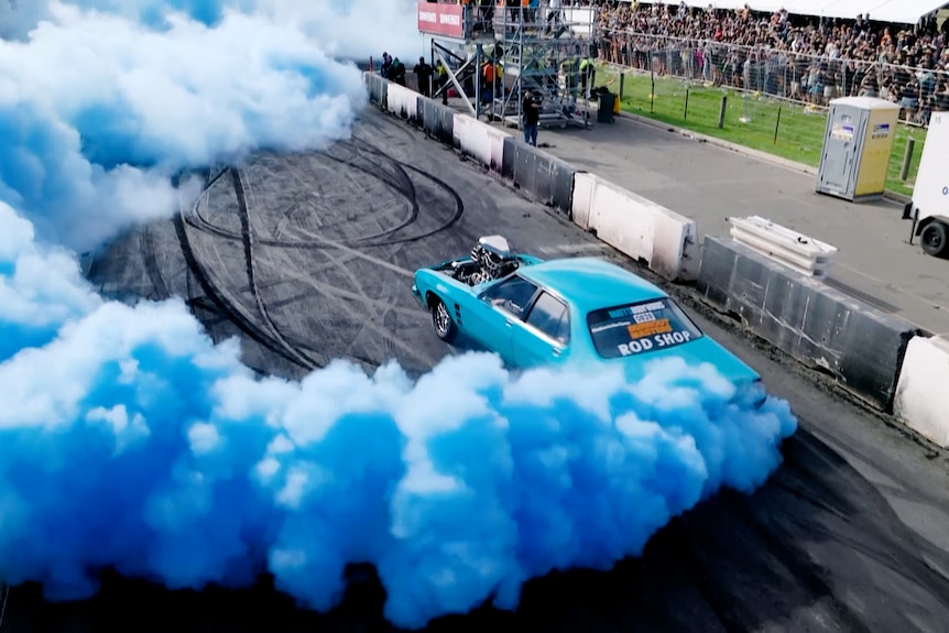 A blue car doing a burnout with blue smoke pouring out the back. 