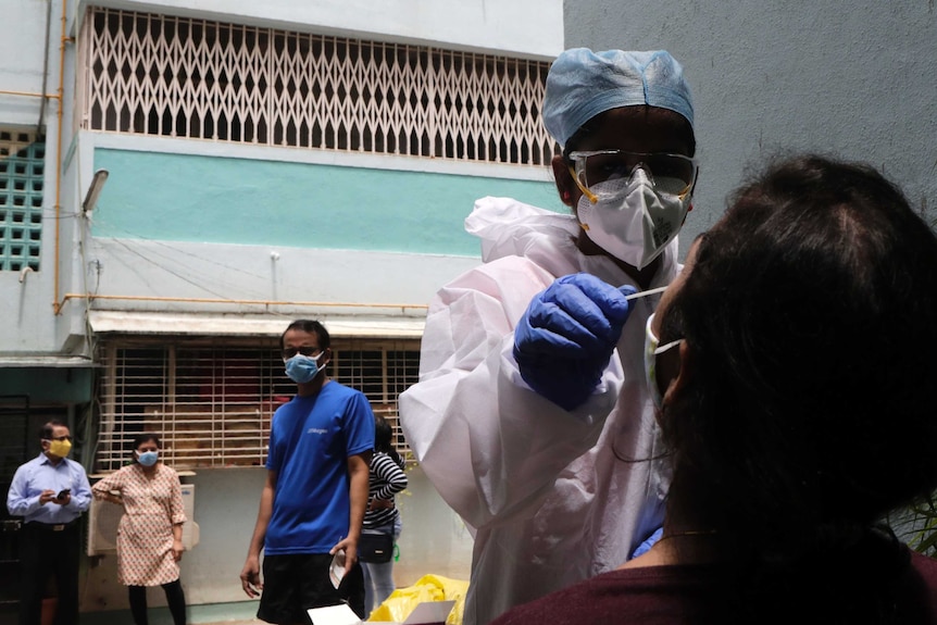 Health workers take swab sample to test for COVID-19 outside a residential building in Mumbai.