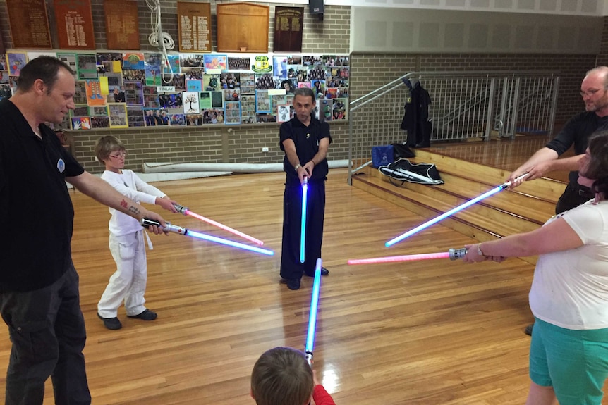 A circle of people holding blue and red lightsabers into the centre