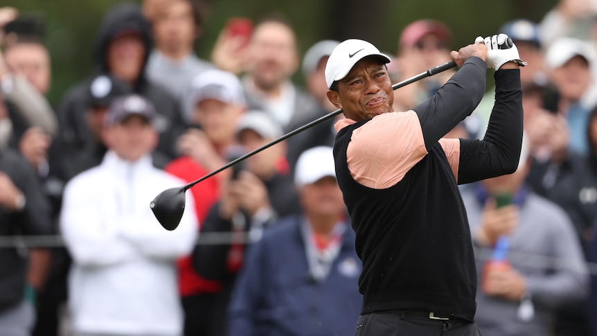 Tiger Woods grimaces as he hits his tee shot.