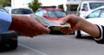 The hand of a young woman takes a wad of cash — Australian $50 and $100 notes — from the hand of an older man.