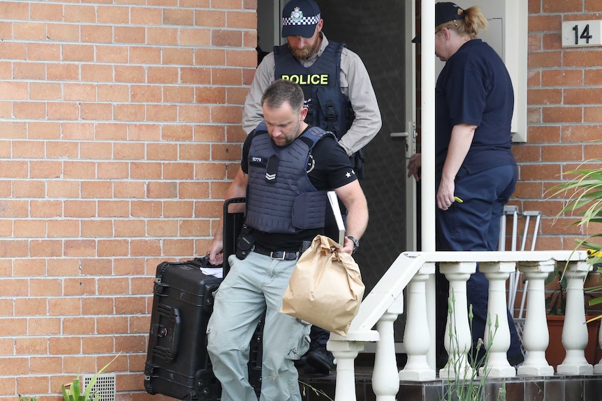 Police officers are seen leaving a house holding bags and luggage.