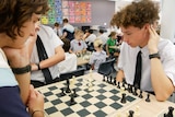 Two teenage boys in school uniform sit at a chess board.