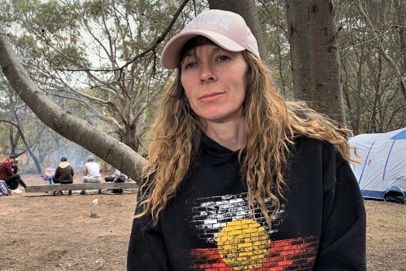 Sharnie Read sits on a log near a campsite.