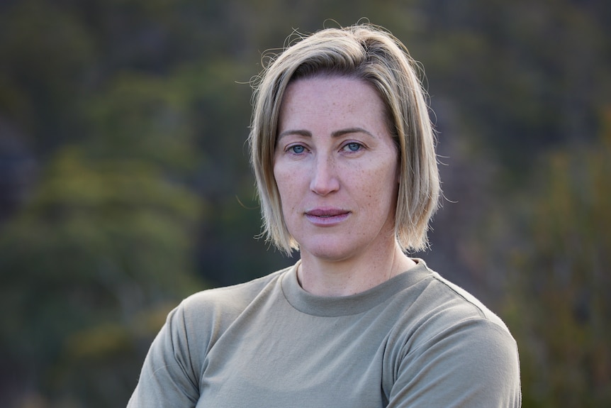 A woman in army colours pants and t shirt sands with arms crossed