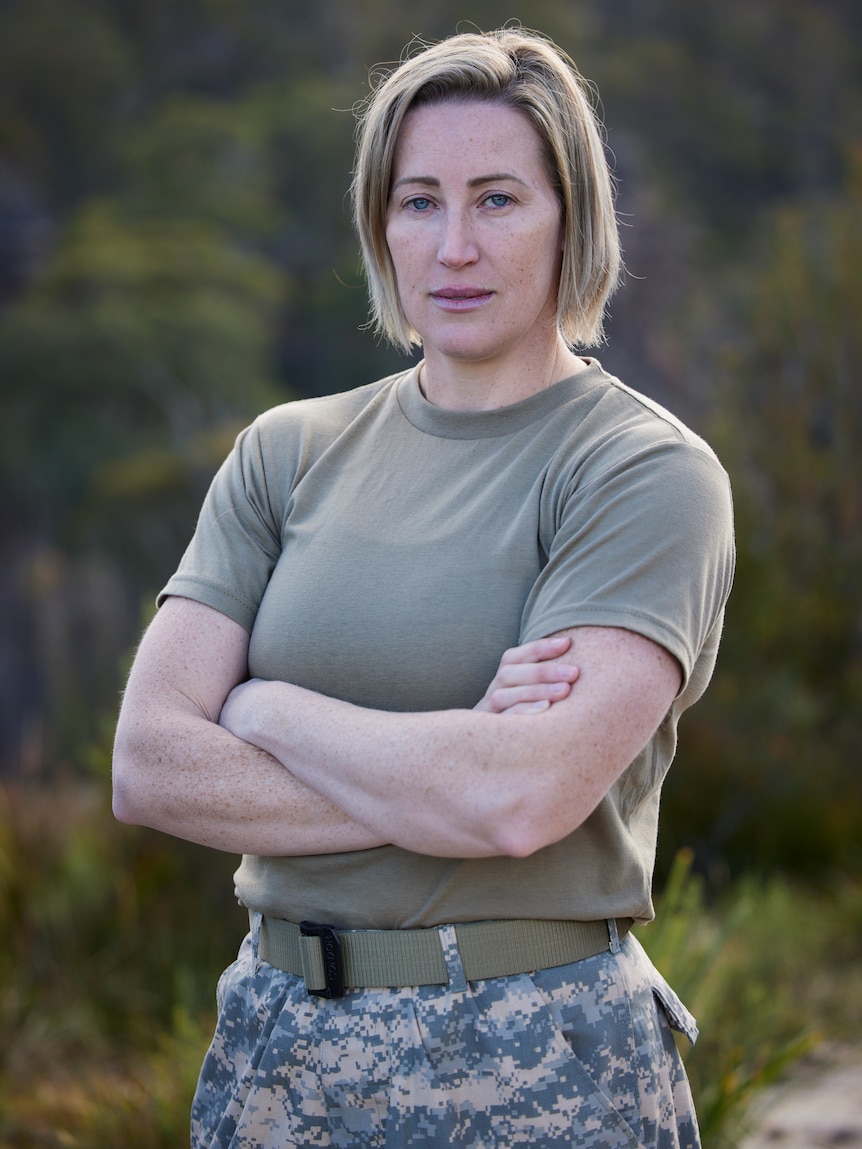 A woman in army colours pants and t shirt sands with arms crossed