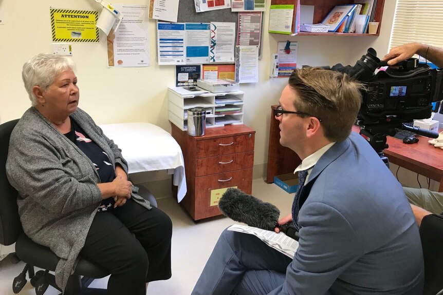 An Aboriginal woman sits in a doctors room speaking to a journalist