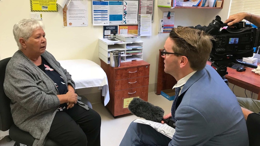 An Aboriginal woman sits in a doctors room speaking to a journalist
