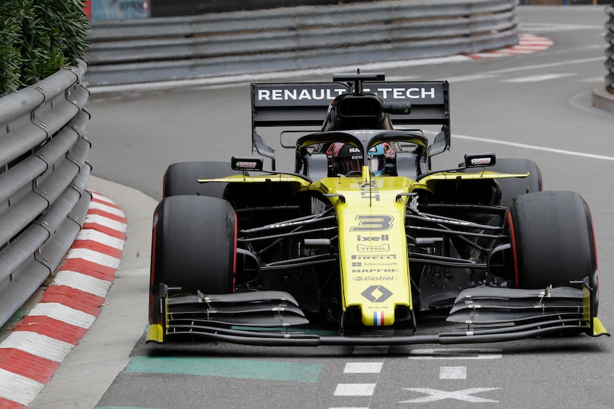 Daniel Ricciardo's yellow F1 car drives close to metal, armco barriers