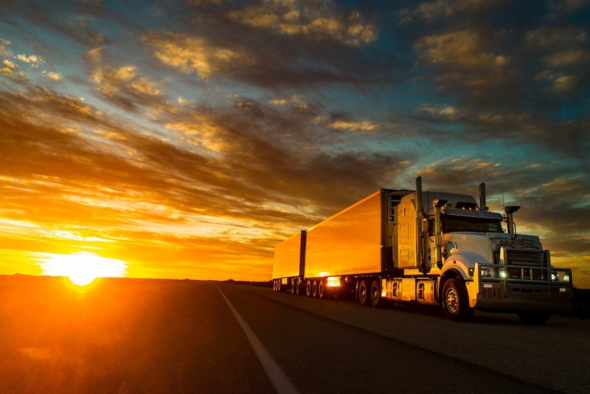 A big rig barrels down an outback highway, the low sun lighting the scene in lambent glory.