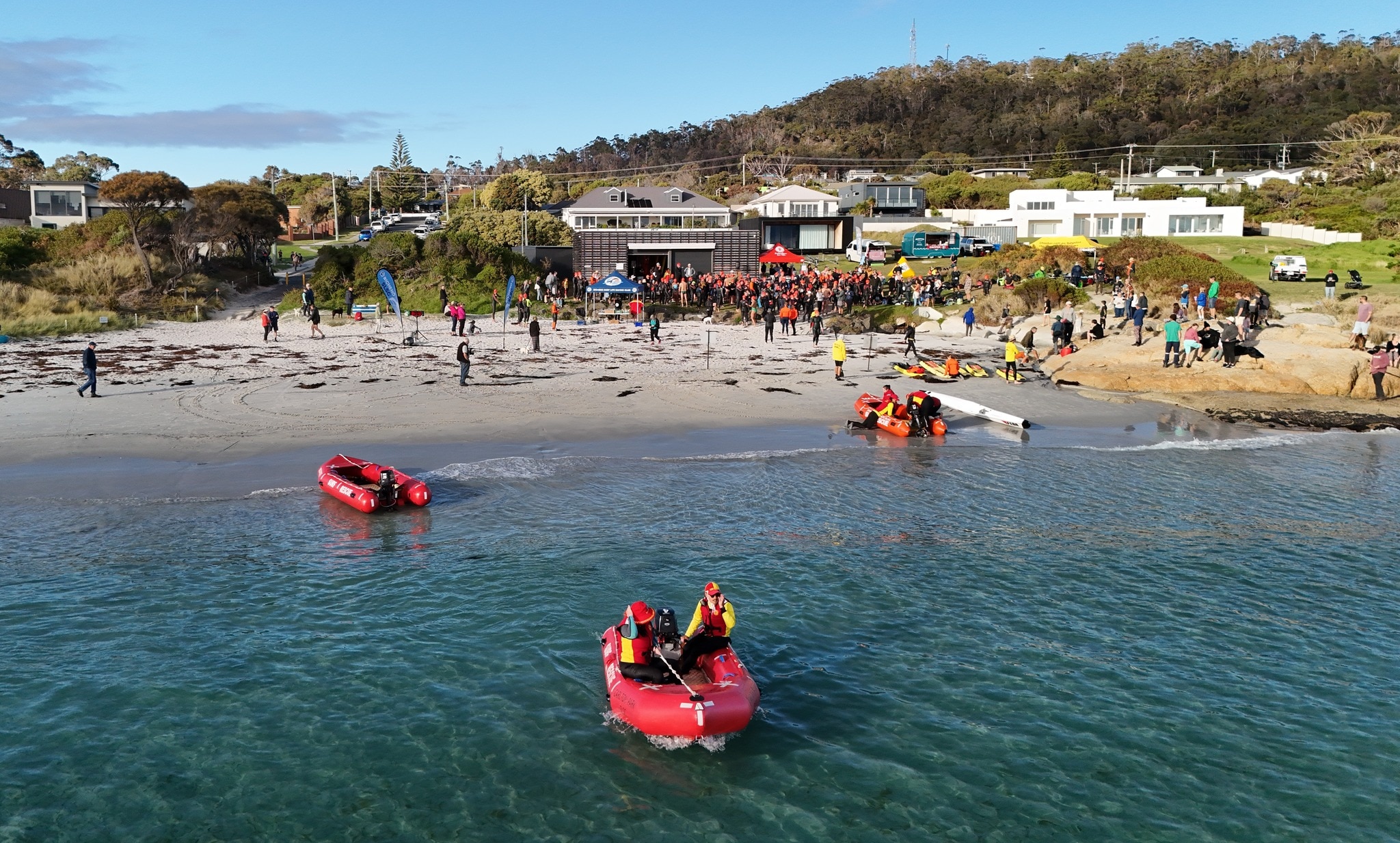 barcos vermelhos na água com centenas de nadadores ao fundo e colinas verdes