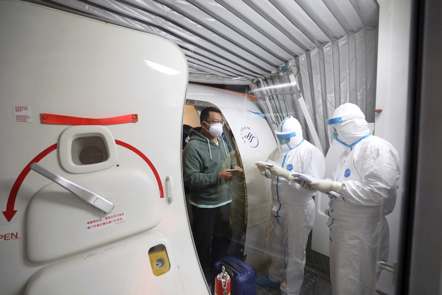 Quarantine workers in protective suits check identity documents as tourists from the Wuhan get off a flight.