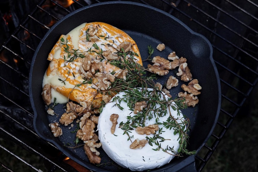 A cast iron frypan with rounds of cheese, walnuts and fresh thyme baked on an open fire.