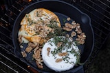 A cast iron frypan with rounds of cheese, walnuts and fresh thyme baked on an open fire.