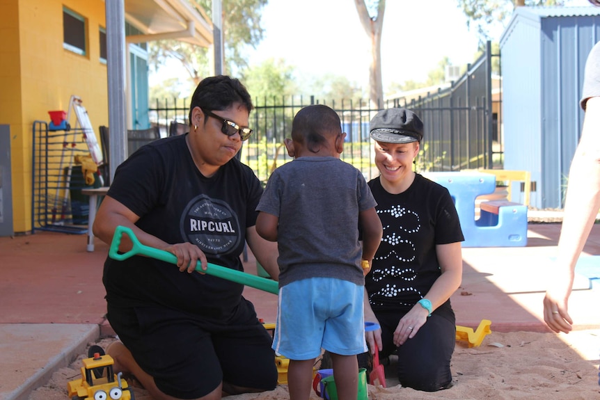 Two women make sand castles with a young Indigenous boy.