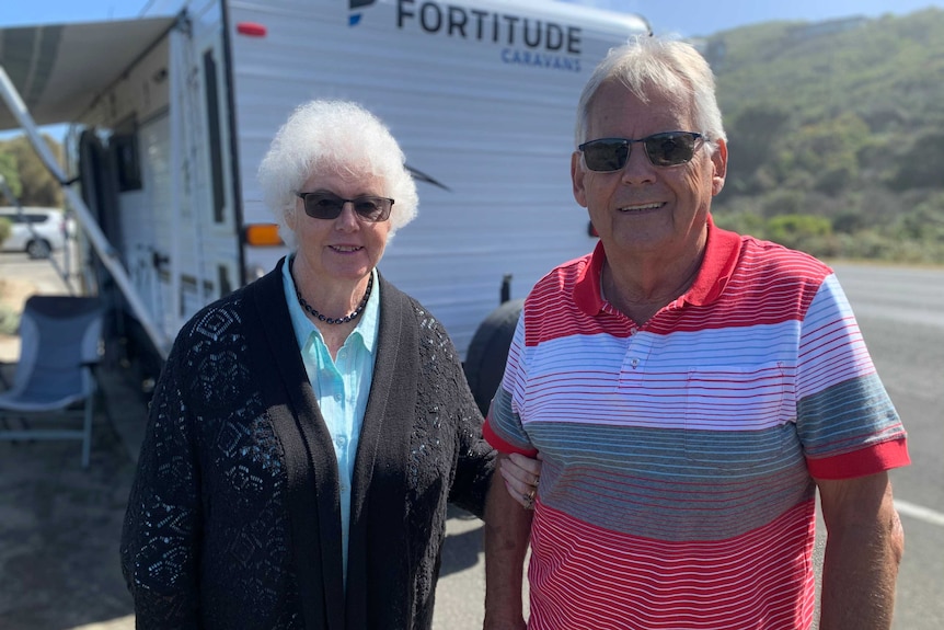 Marilyn Halladay and Ian Halladay smile at the camera with a caravan in the background.