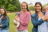 Three women hold newborn babies in a leafy park in London.