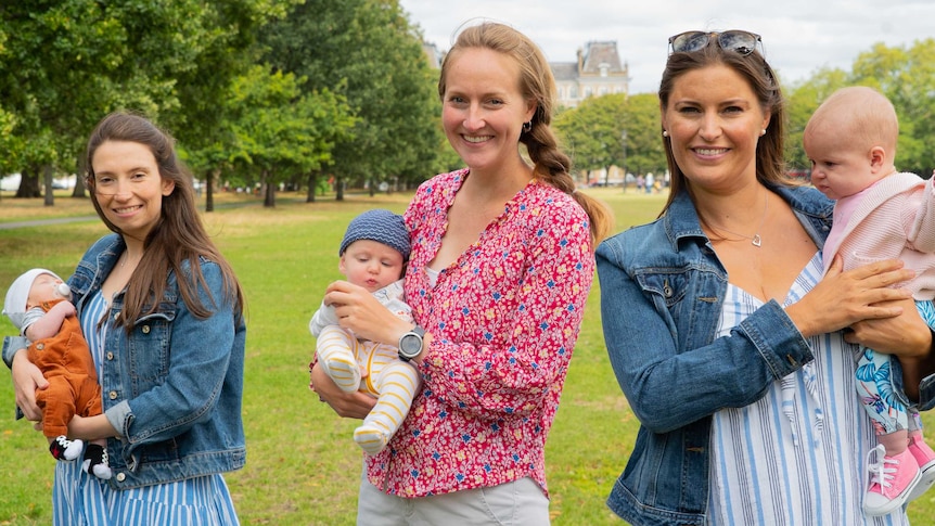 Three women hold newborn babies in a leafy park in London.